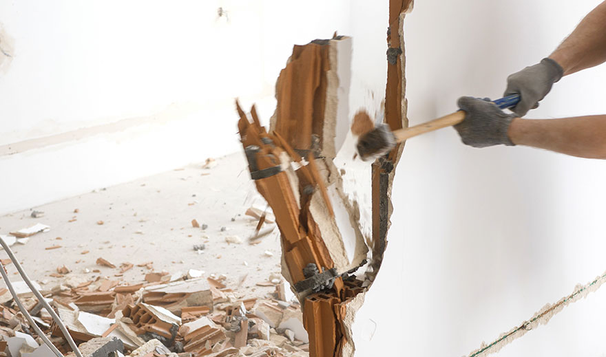 Mann schlägt mit einem Hammer auf eine Mauer, Wandabriss